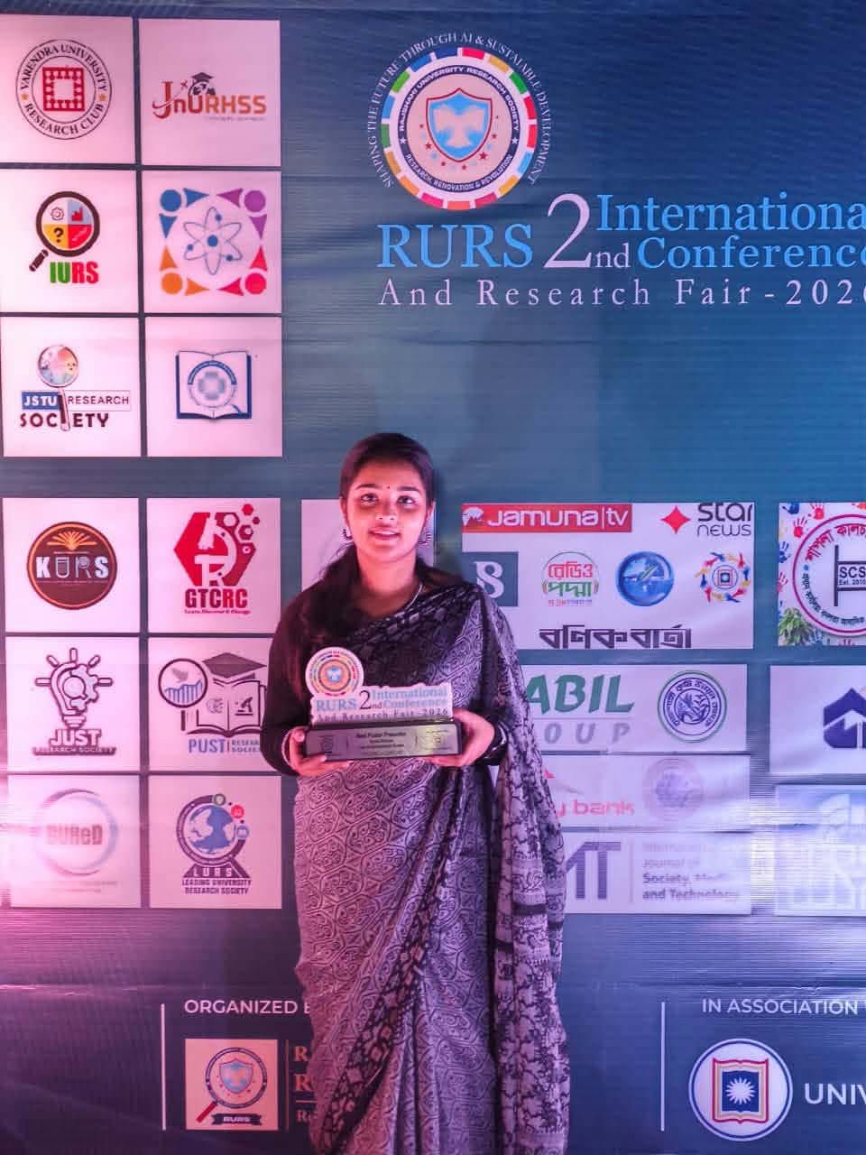 Noshin Tasnim holding the award in front of the RICRF conference backdrop